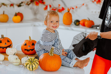 Baby girl is sitting on decorated table with pumpkins near her mom.