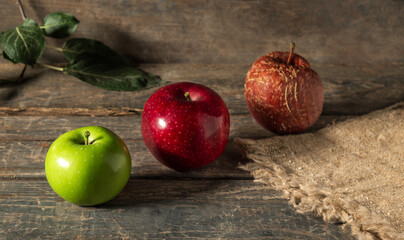 Green, red and rotten apples on burlap on wooden boards.