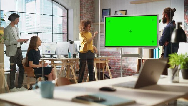 Positive Businesswoman Leading a Team Meeting in Creative Office Conference Room. Excited Multiethnic Woman Showing Presentation on Green Screen Mock Up Chroma Key Monitor.