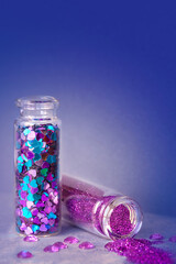 All kinds of glitter products on pink sparkling background. Close-up on vials, bottles with various glitter makeup in pink, blue and turquoise shades. Shallow DOF, focus on scattered violet glitter.