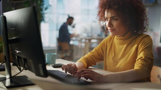 Close Up Portrait of a Happy Middle Eastern Manager Working in Creative Office. Young Stylish Female with Curly Hair Using Laptop Computer in Marketing Agency. Cinematic Footage Through a Glass Wall.