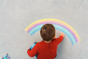 Child drawing rainbow with colorful chalks on ground or asphalt on summer sunny day. Cute boy having fun. Peace, freedom concept - 530567028