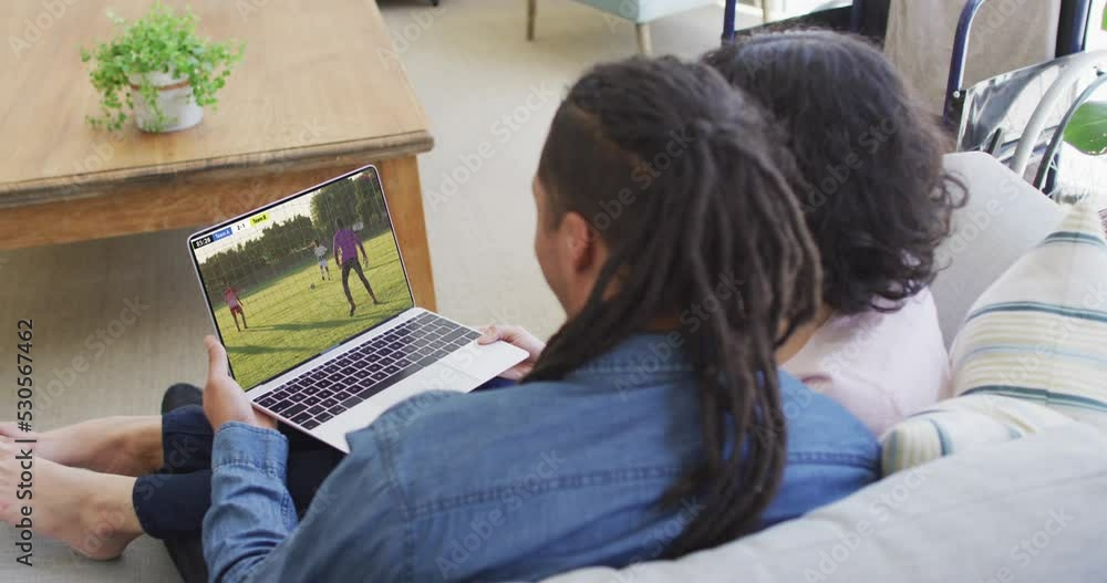 Wall mural Biracial couple laptop with diverse male soccer players playing match on screen