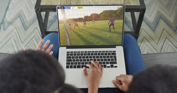 Hands using laptop with diverse male soccer players playing match on screen