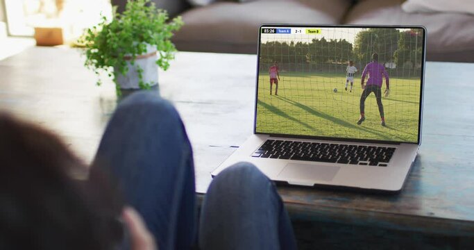 Man using laptop with diverse male soccer players playing match on screen