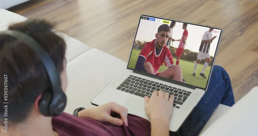 Sticker Caucasian teenager using laptop with diverse male soccer players playing match on screen