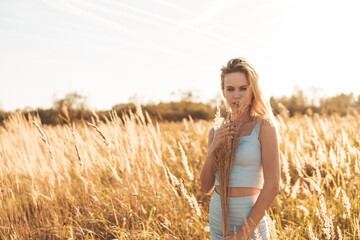 Beautiful blonde woman on a walk in a field with dry grass. A walk in nature, sunset in a field of...