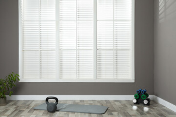 Exercise mat with different dumbbells and kettlebell in spacious room