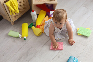 Cute baby playing with cleaning supplies on floor at home, above view. Dangerous situation