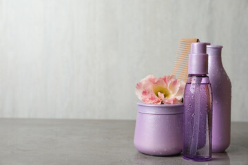 Different hair products, flower and wooden comb on grey table. Space for text