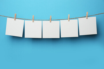 Wooden clothespins with blank notepapers on twine against light blue background. Space for text