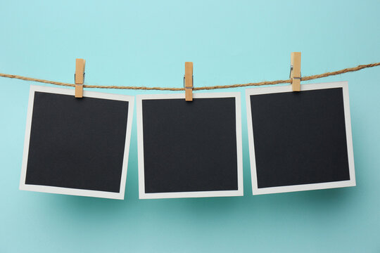 Wooden clothespins with empty instant frames on twine against light blue background. Space for text