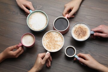 People holding different cups with aromatic hot coffee at wooden table, top view
