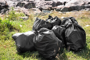 Many trash bags full of garbage on green grass outdoors. Environmental Pollution concept