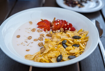 Yogurt bowl with fresh sliced strawberries and dry corn flakes. Breakfast cereal toppings served with spoon on the wooden table. Traditional corn flakes breakfast concept. Healthy eating concept