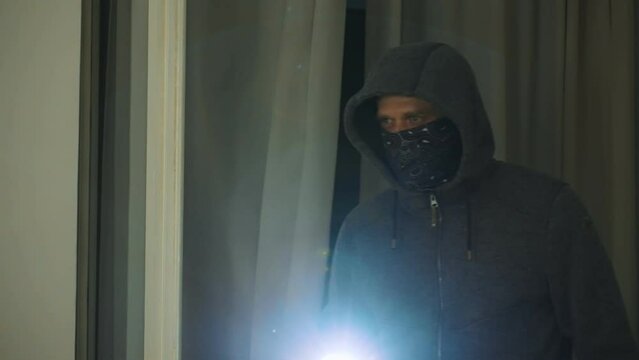 Masked robber with flashlight torch checking apartment.