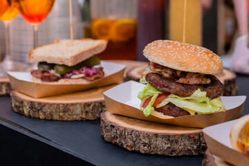 Fresh large burger with meat cutlet and sandwich on wooden board on counter for sale at summer local food market - close up view. Outdoor cooking, gastronomy and street food concept