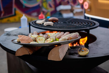 Meat sausages and zucchini slices on plate on brazier at outdoor summer local food market - close up. Gastronomy, cookery and street food concept