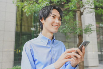 Fototapeta premium オフィス街でスマートフォンを操作するビジネスマン