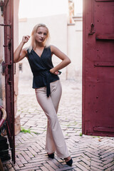 a blonde beautiful girl in sunglasses, a black blouse and beige pants poses against the background of an old collar