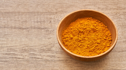 a pile of ground turmeric powder or curcumin powder in wood plate on wooden table background. turmeric or curcumin powder background                                                                 