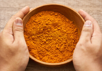 man hand holding a pile of ground turmeric powder or curcumin powder in wood plate on wooden table background. turmeric or curcumin powder background