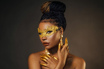 Portrait sexy african woman face close up in golden venetian carnival mask. Girl fashion model perfect skin, golden evening holiday makeup, glitter diamond stones lip gloss, hands in gold liquid paint - obrazy, fototapety, plakaty