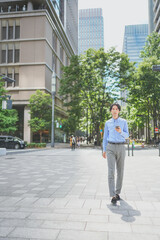 Fototapeta na wymiar スマートフォンを操作しながらオフィス街を歩くビジネスマン