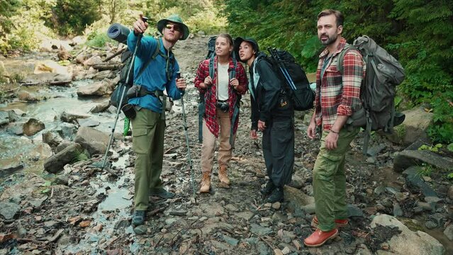 Positive multiethnic tourists friends pointing to the side and talking in the mountains outdoors
