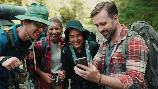Smiling multiethnic tourists friends looking at phone and talking in the mountains outdoors