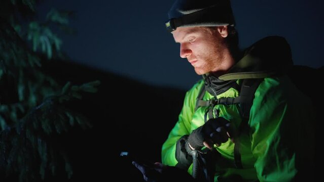 Concentrated red haired tourist man looking at phone and around in the mountains at night