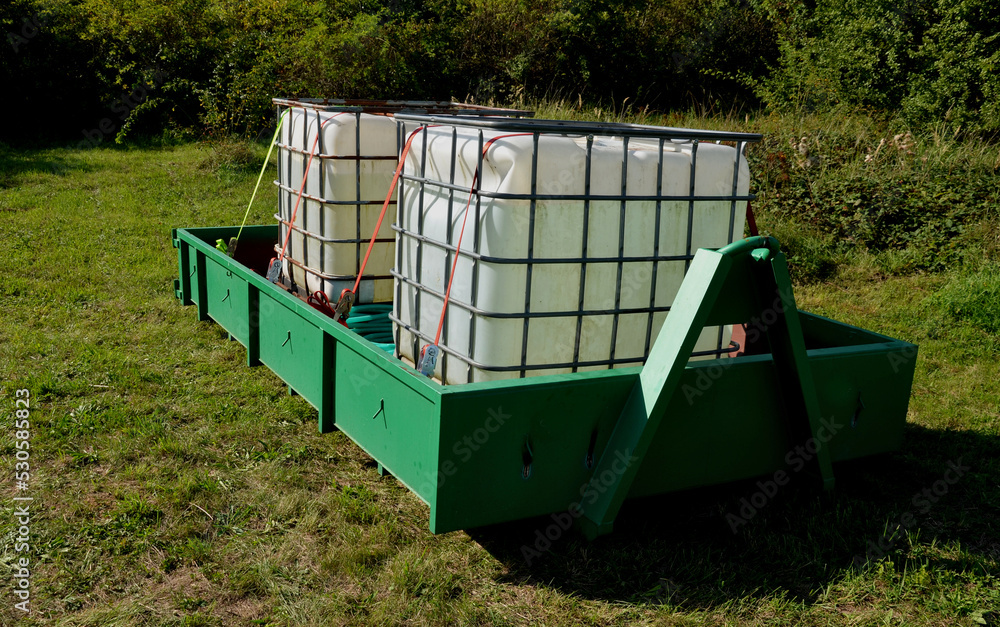 Wall mural two plastic containers in a metal cage. full of water for watering or drinking livestock in hot weather. the car pulls the container onto the rear wheel. arrange a delivery of chemicals or fuel. agro 