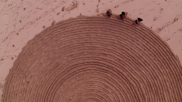 Aerial view of people trampling down mysterious spiral half circus on sand. Fake mystery and sports exercise for tourists on seaside. Rite with ancient symbol. Enigmatic sign on sandy beach in summer.