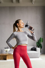 Keep hydrated. Young woman drinking water on yoga mat at home