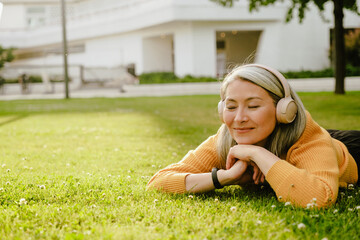 Grey asian woman smiling while lying on grass in summer park