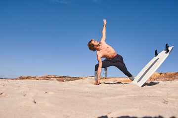 Shirtless man standing on the sand near the sea and stretching