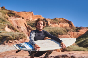 Caucasian surfer kneeling in front of the ocean with his board at the hands