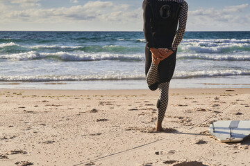 Fototapeta na wymiar Athletic male surfer doing stretches for his legs near the ocean