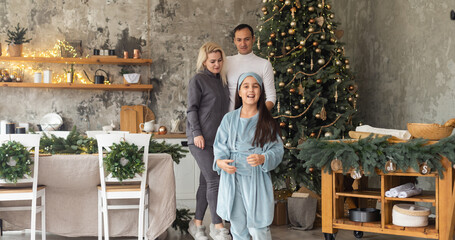 beautiful Christmas tree at home. Parents presenting gift box to charming daughter.