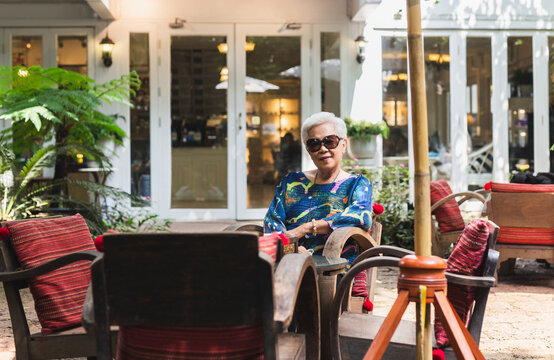 Portrait of senior woman in sunglasses sitting on a chair in cafe outdoor.