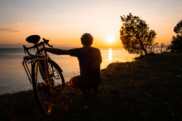 Fototapeta na wymiar Cyclist hugs his bicycle and enjoy sunset over calm tranquil lake. Solitude and love bicycle outdoors concept
