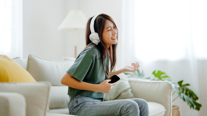 Young asian woman listening to music on couch in living room at home. Happy asia female using...