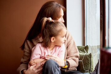 Fototapeta premium Little caucasian girl with mother looking at window and dreaming. A lot of gift boxes around. Happy family christmas concept