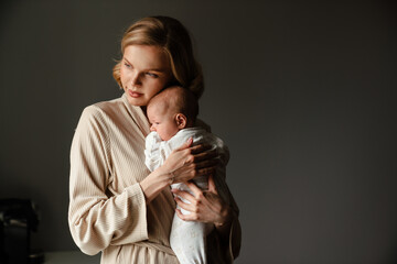 Young white mother wearing housecoat holding her baby in her arms