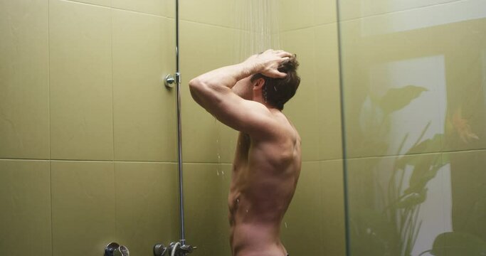 Black-haired guy washes muscular body in glass shower