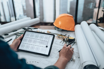 Engineering working with drawings inspection on tablet in the office and Calculator, triangle ruler, safety glasses, compass on Blueprint. Engineer, Architect, Industry and factory concept.