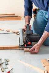 carpenter performing cutting action with electric wood cutting machine and kneeling posture
