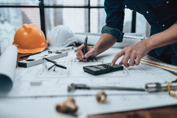 Engineering working with drawings inspection and writing on the office desk and Calculator, triangle ruler, safety glasses, compass on Blueprint. Engineer, Architect, Industry and factory concept.