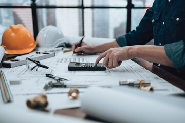 Engineering working with drawings inspection and press calculator on the office desk and triangle ruler, safety glasses, compass on Blueprint. Engineer, Architect, Industry and factory concept.