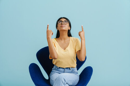 Young Beautiful Indian Woman In Glasses Looking And Pointing Upwards